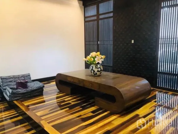 Condominium for rent in Pathum Wan, Bangkok - Minimalist lounge with a sculptural wooden coffee table, glossy striped wood flooring and slatted feature doors.