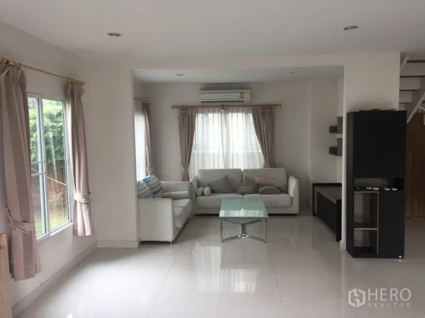 Detached House for rent in Pathum Thani - Bright living room with white sofas, glass coffee table, large windows and glossy tile floors.