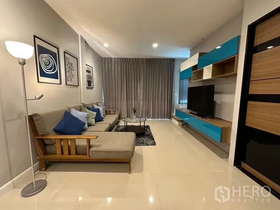 Townhouse for rent in Chom Thong, Bangkok - Another angle of the living room showing sectional sofa, TV wall cabinet and full-height curtains.