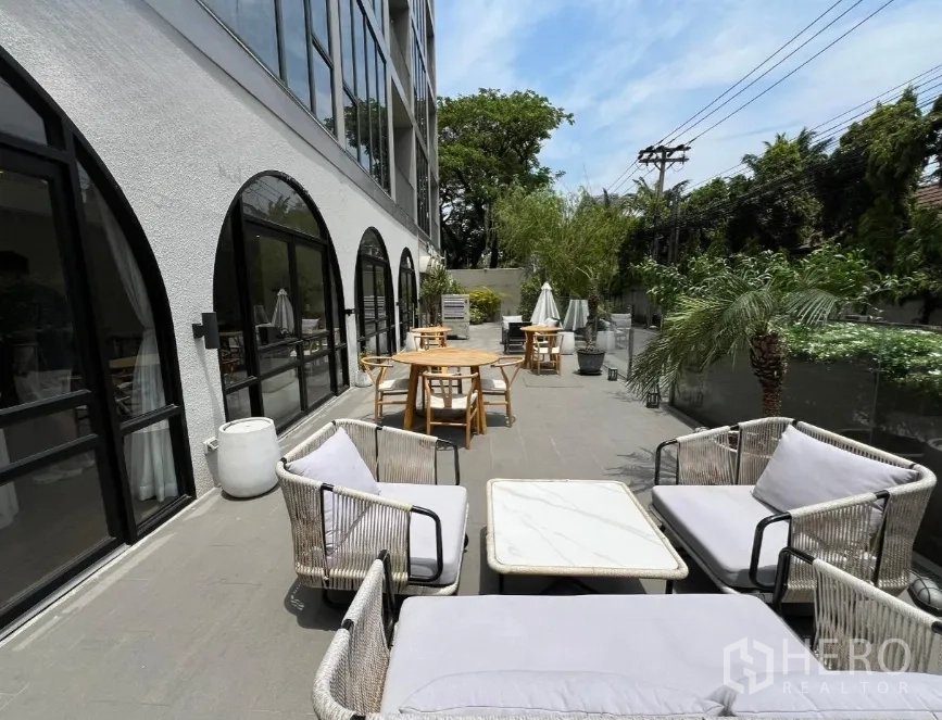 零售空间 出租在Watthana, Bangkok - 沿建筑的户外露台，设有休闲沙发、咖啡桌与绿植，旁为拱形落地窗。