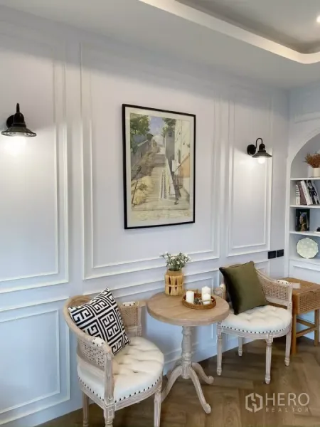 独立式住宅 出售在Sai Mai, Bangkok - 温馨角落，两把软垫椅与圆形木桌，墙面线条装饰。