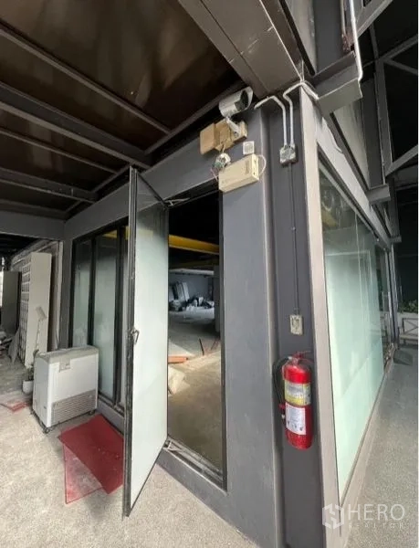 零售空间 出租在Watthana, Bangkok - 建筑转角入口处，玻璃门敞开，可见灭火器与外露管线。