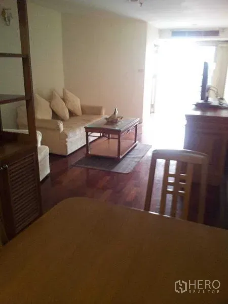 คอนโด ให้เช่า - มุมนั่งเล่นพร้อมโซฟาสีครีม โต๊ะกลาง และทีวี พื้นไม้เงางาม