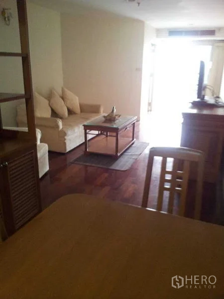 คอนโด ให้เช่า - มุมนั่งเล่นพร้อมโซฟาสีครีม โต๊ะกลาง และทีวี พื้นไม้เงางาม