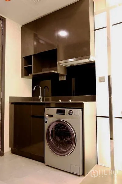 Condominium for rent in Watthana, Bangkok - Compact kitchen with glossy cabinets, sink, range hood and front-loading washer.