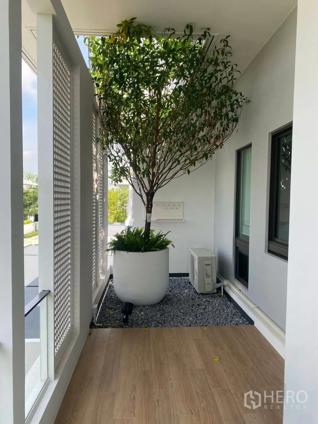 บ้านเดี่ยว for rent or sale in Bang Phli, Samut Prakan - ชานพักคลุมหลังคาพื้นลายไม้ ม่านระแนงสีขาว และกระถางต้นไม้ขนาดใหญ่.