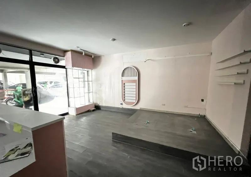店屋 出租在Watthana, Bangkok - 主营业空间，大面积展示窗，灰色地砖、抬高平台与接待柜台。
