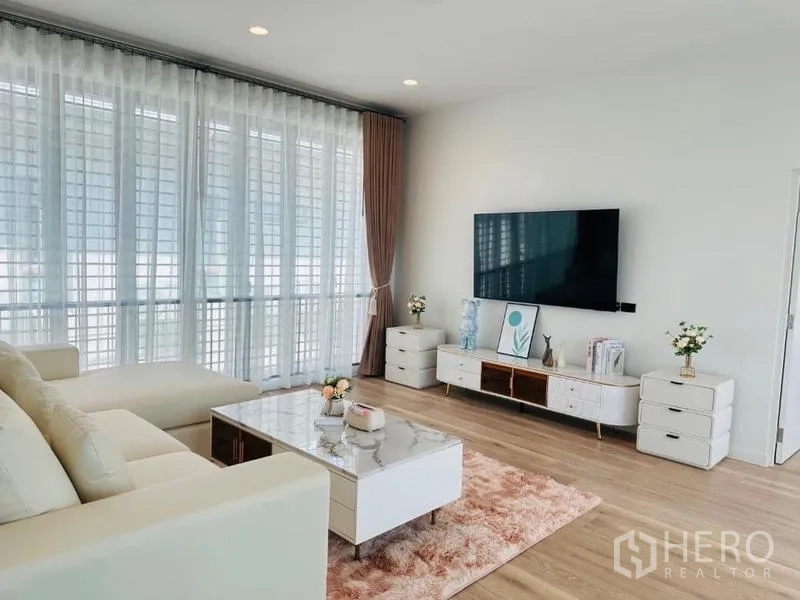 บ้าน ให้เช่าหรือขายในBang Kapi, Bangkok - อีกมุมของห้องนั่งเล่น เห็นผนังทีวี พรมสีชมพู และหน้าต่างขนาดใหญ่รับแสง.