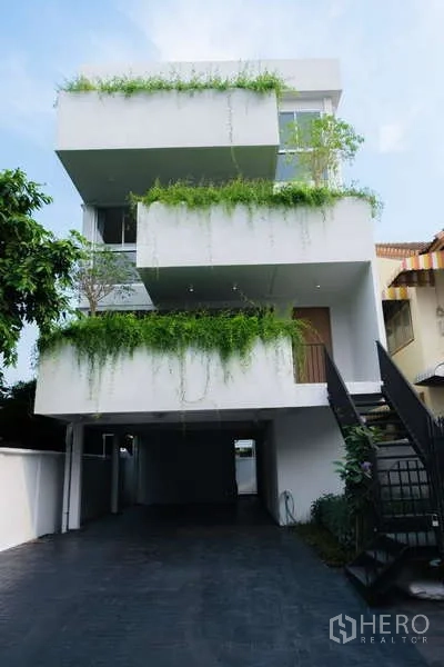 Home Office for rent in Phra Khanong, Bangkok - Modern three-storey home office facade with cantilevered balconies draped in greenery and a long driveway.