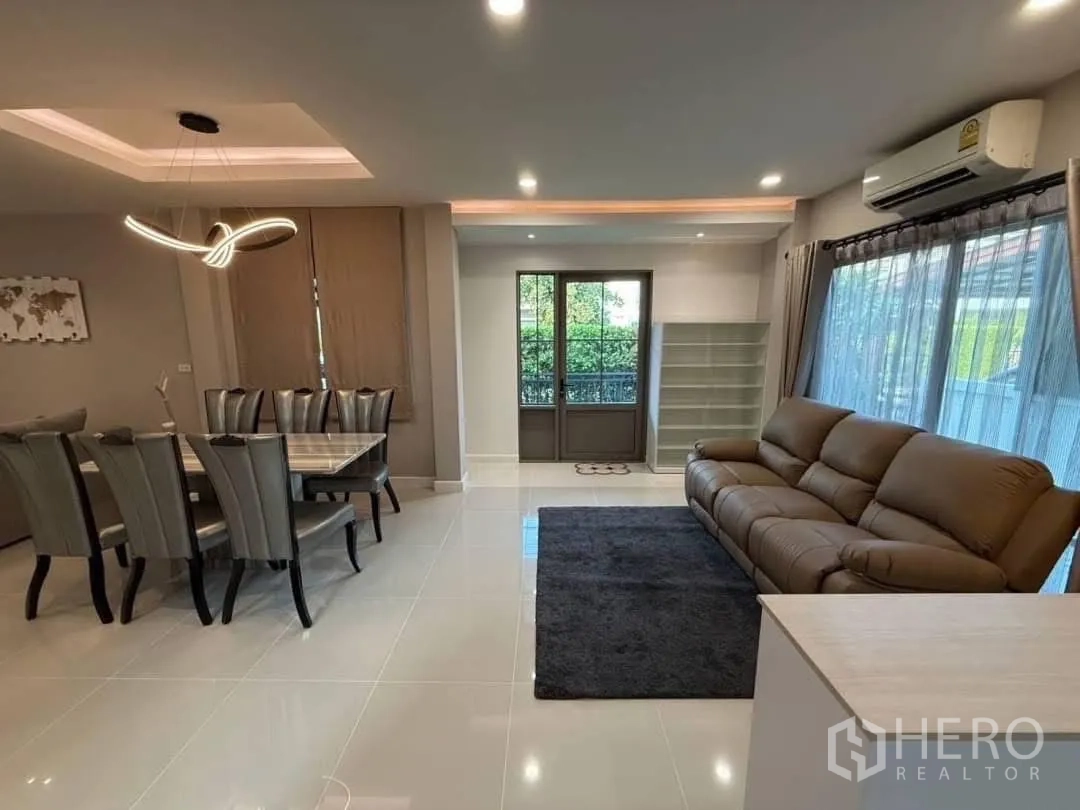 Detached House for rent in Prawet, Bangkok - Open-plan living and dining with leather sofa, air conditioner and garden-view windows.