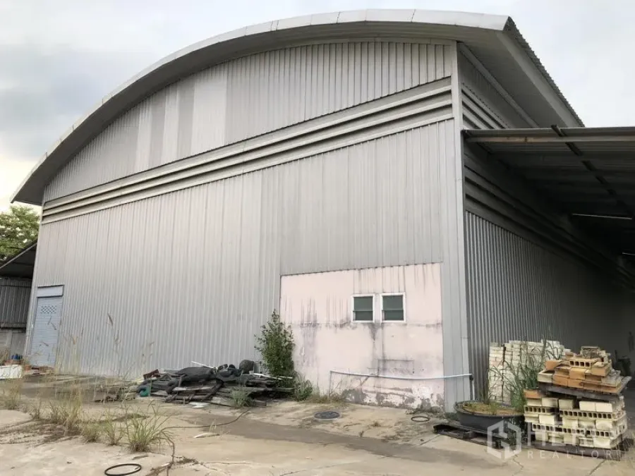คลังสินค้า ให้เช่าหรือขายในLam Luk Ka, Pathum Thani - มุมมองด้านข้างโกดังโครงสร้างเหล็ก หลังคาโค้ง กันสาดข้าง ประตูบริการ และพื้นที่เก็บของกลางแจ้งบนพื้นคอนกรีต