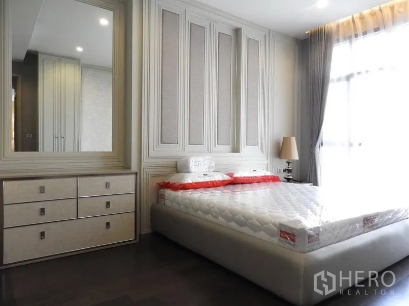 公寓 出租在Watthana, Bangkok - 采光充足的卧室，墙面饰板、大镜子、抽屉柜与薄纱窗帘。