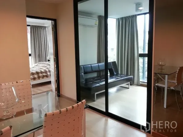 คอนโด ให้เช่าหรือขายในChatuchak, Bangkok - กั้นกระจกบานเลื่อนเปิดสู่ห้องอเนกประสงค์สว่าง พร้อมโซฟาสีดำและห้องนอนถัดไป