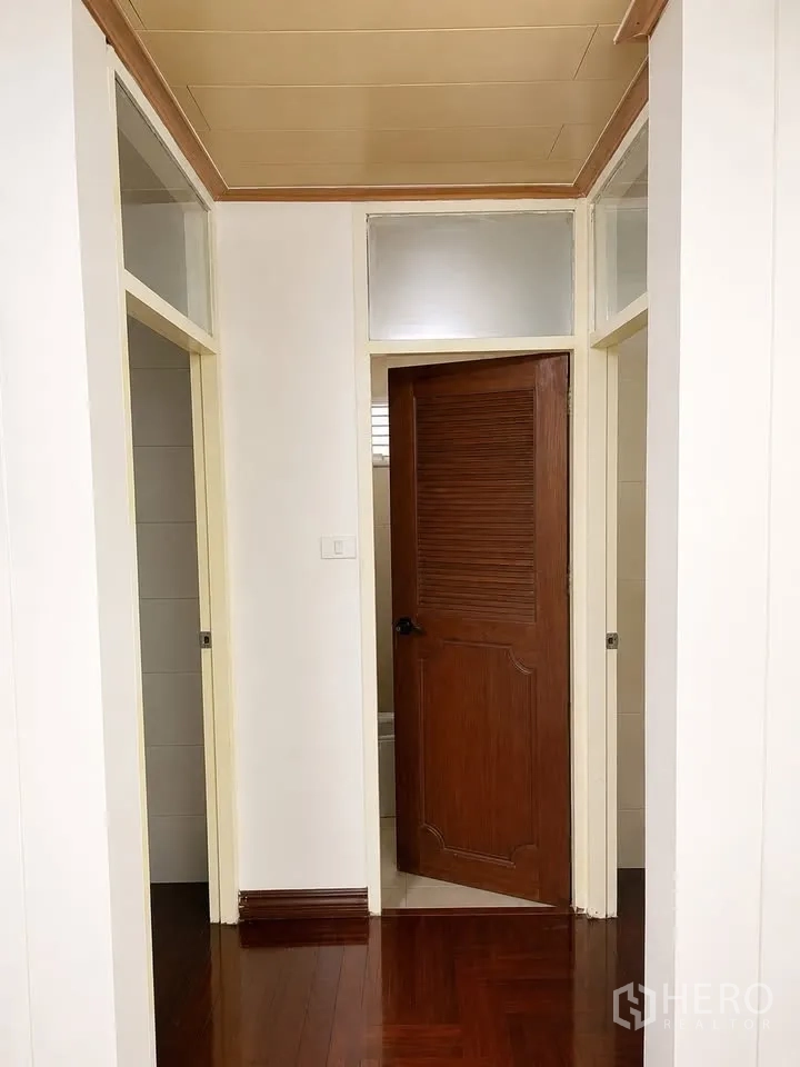 Detached House for rent in Prawet, Bangkok - Hallway with wooden door, white walls and parquet flooring.