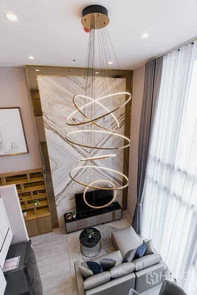 公寓 出租在Phra Khanong, Bangkok - 挑高客厅，造型吊灯与大理石特色墙，旁有通高落地窗。