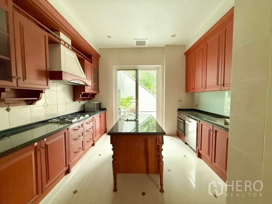 Townhouse for rent in Bang Kho Laem, Bangkok - Western kitchen with red wood cabinetry, black stone counters and an island opening to a garden view