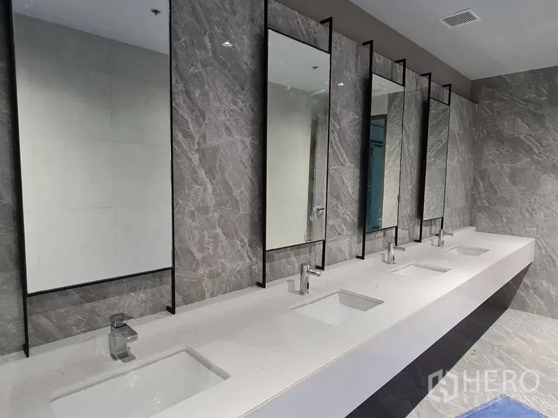 Office Space for rent - Row of rectangular sinks with tall framed mirrors set against a gray marble wall in the office washroom.