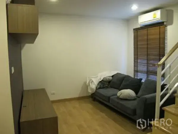 ทาวน์เฮาส์ ให้เช่าหรือขายในWang Thonglang, Bangkok - มุมนั่งเล่นพื้นไม้ โซฟาสีเทา ตู้บิลต์อิน ม่านปรับแสง และเครื่องปรับอากาศ