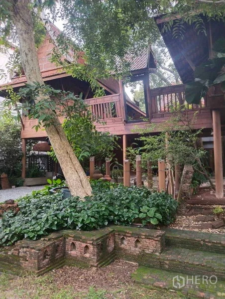 Detached House for rent or sale in Suan Luang, Bangkok - Connected Thai stilt houses framed by mature greenery and brick-edged garden beds.