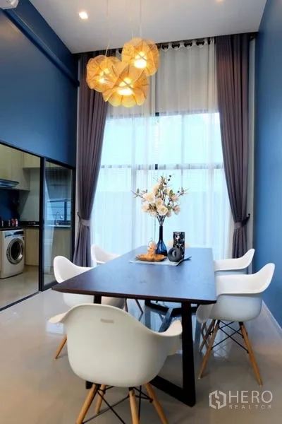 Townhouse for rent in Khlong Toei, Bangkok - Double-height dining area with pendant lights, dark wood table and white chairs beside tall draped windows.