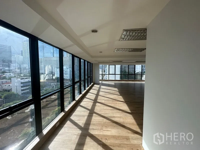 Office Space for rent in Sathon, Bangkok - Open-plan office corridor lined with floor-to-ceiling windows and wood floors overlooking the Bangkok skyline.