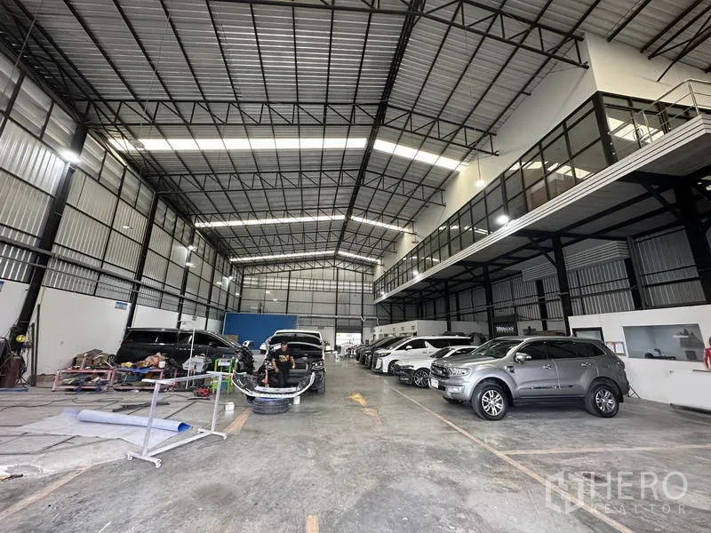 货栈 出租在Bang Khen, Bangkok - 明亮的仓库车间，停放多辆车，一侧为长条夹层办公室。