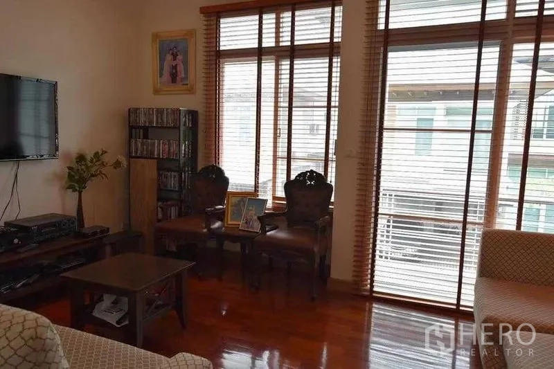Detached House for sale in Bueng Kum, Bangkok - Living area with TV, classic chairs, big windows with blinds and polished wood flooring.