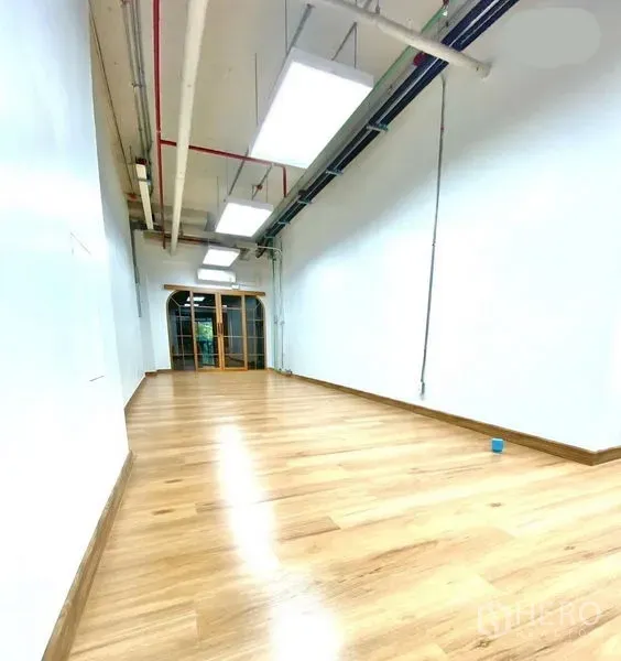 Office Space for rent in Khlong Toei, Bangkok - Long open‑plan office with wood floors, suspended LED panels and arched glass entry.