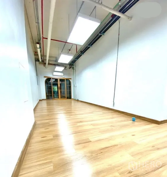 Office Space for rent in Khlong Toei, Bangkok - Long open‑plan office with wood floors, suspended LED panels and arched glass entry.