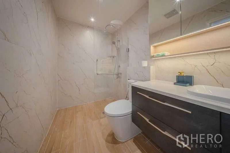 คอนโด ให้เช่า - ห้องน้ำมุมกว้าง มีฝักบัวเรนชาวเวอร์ โถสุขภัณฑ์ และชั้นกระจกไฟส่องสว่าง
