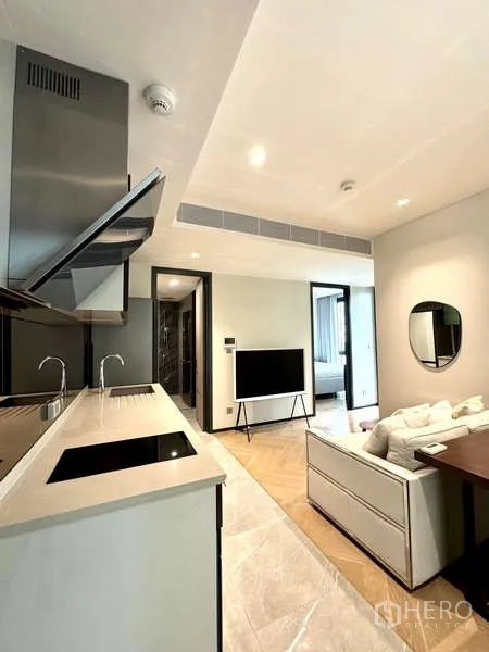 Condominium for rent in Watthana, Bangkok - Sleek kitchen with long countertop and induction hob facing TV and sofa.