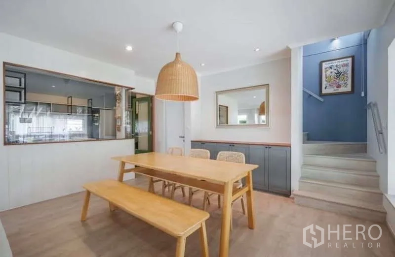 Detached House for rent in Prawet, Bangkok - Dining area with wooden table and bench, woven pendant light and kitchen pass-through.