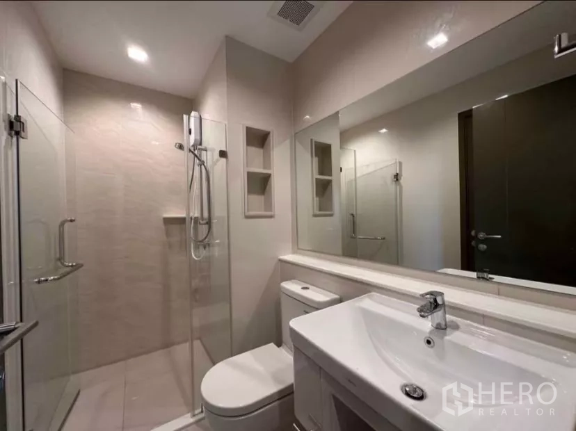 Condominium for rent in Chatuchak, Bangkok - Contemporary bathroom with glass-enclosed shower, vanity, and toilet.