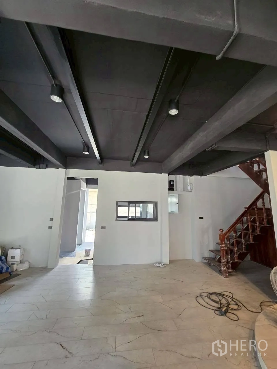 Detached House for rent in Phra Khanong, Bangkok - Open-plan living area with exposed beams, white walls, and the wooden stairs.