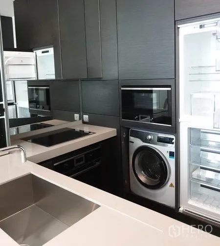 Condominium for rent in Pathum Wan, Bangkok - Contemporary kitchen with built-in oven, induction hob, stainless sink, refrigerator and washing machine.