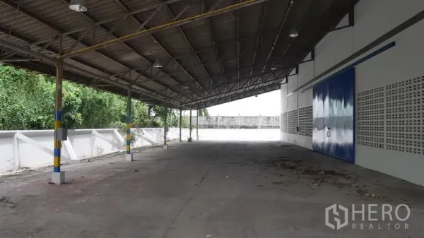 Factory for rent in Khlong Sam Wa, Bangkok - Covered loading bay with steel roof, blue sliding door and wide concrete yard at a Bangkok factory.