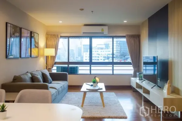 Condominium for rent in Pathum Wan, Bangkok - Bright living room with large window, city view, sofa and TV unit.
