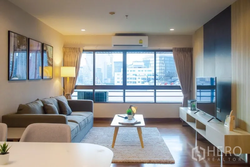 Condominium for rent in Pathum Wan, Bangkok - Bright living room with large window, city view, sofa and TV unit.