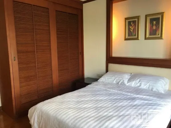 Condominium for rent in Khlong Toei, Bangkok - Cozy bedroom with wooden built-in wardrobe and a queen bed with framed artwork.