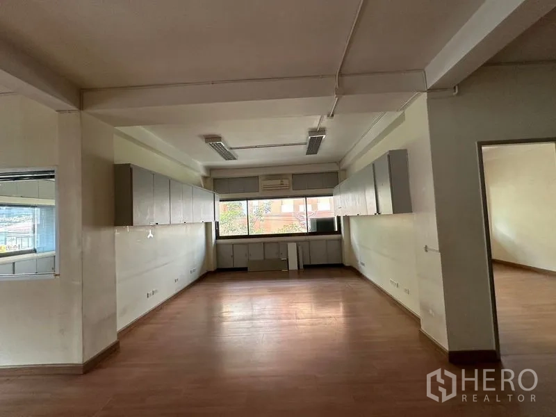 Office Space for rent in Khlong Toei, Bangkok - Open-plan office area with a large window, overhead fluorescent lights, and wall-mounted cabinets.