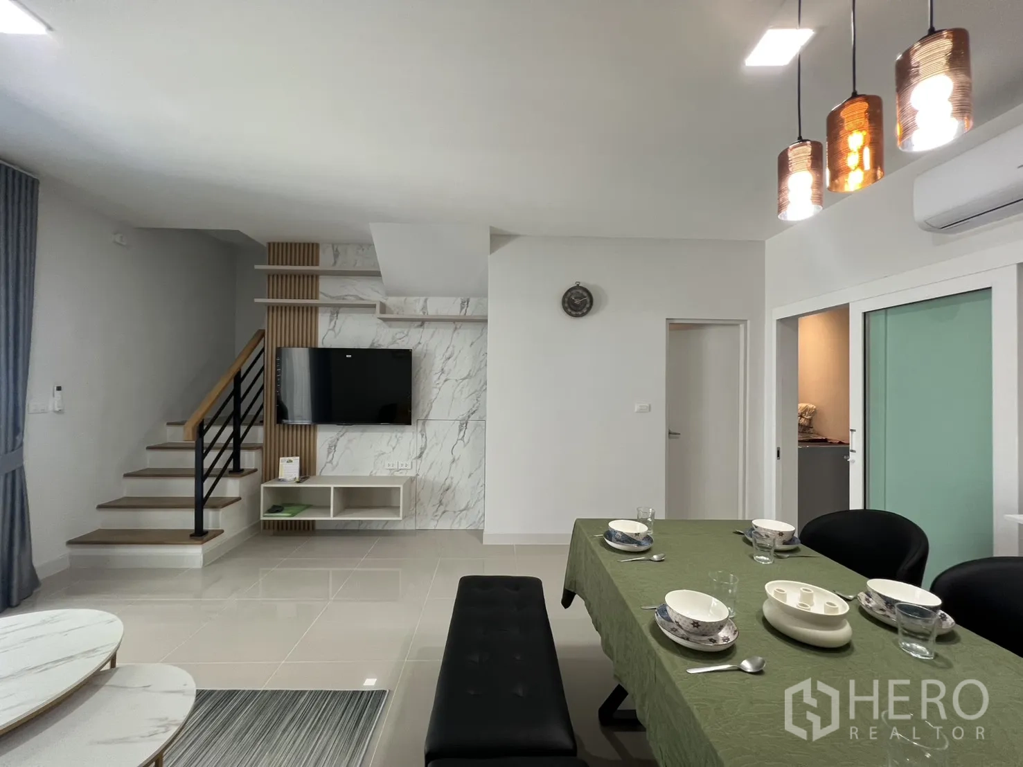Townhouse for rent in Bang Phli, Samut Prakan - Open-plan living and dining area with TV wall, staircase and pendant lights.