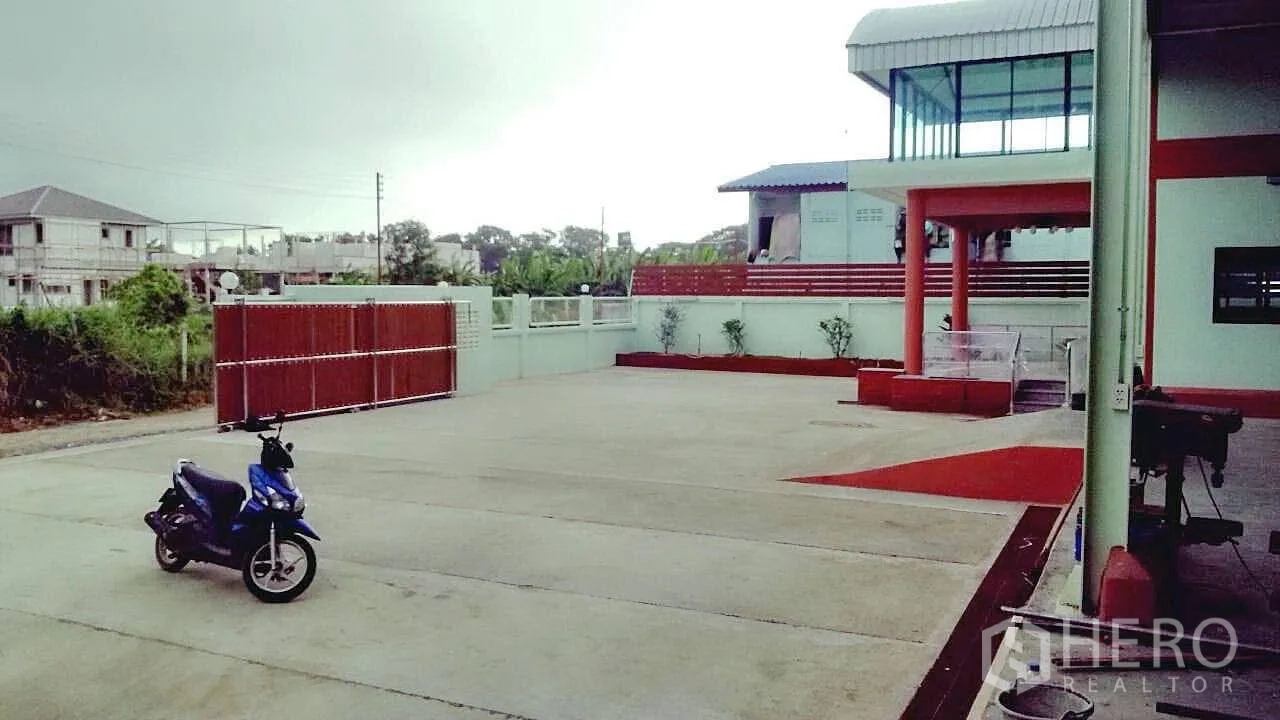 โรงงาน ขายในPathum Thani - ลานคอนกรีตกว้างหน้าตัวอาคาร พร้อมประตูรั้วบานเลื่อนสำหรับรถบรรทุก