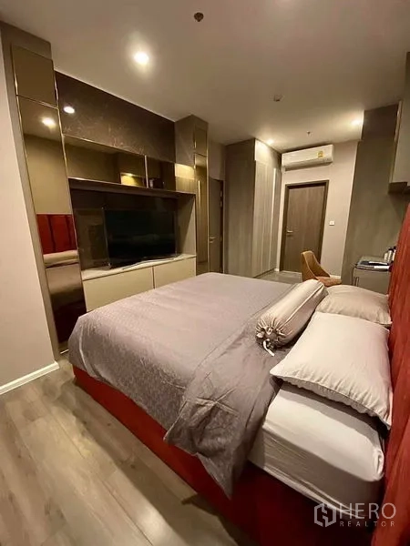Condominium for rent in Phra Khanong, Bangkok - Cozy bedroom with red upholstered headboard, built-in wardrobe and large TV cabinetry.