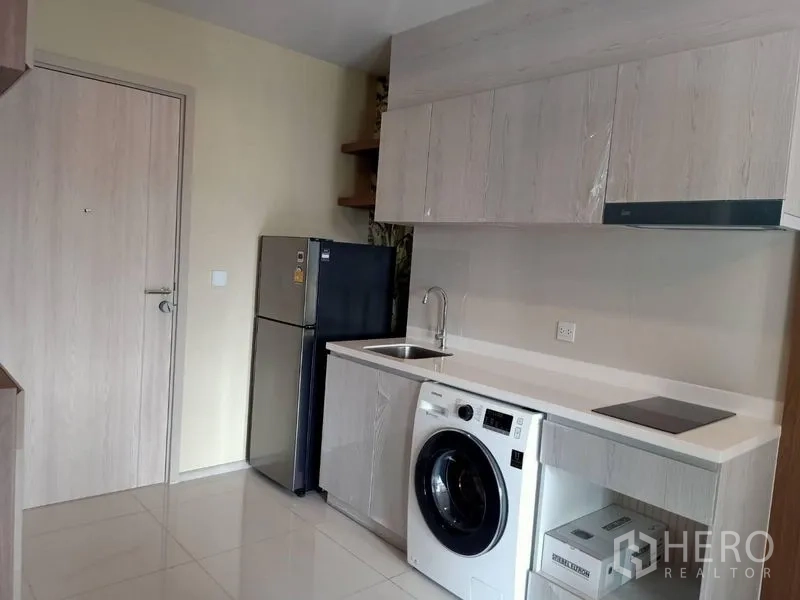 Condominium for rent in Pathum Wan, Bangkok - Modern kitchen with white cabinets, sink, fridge, electric cooktop and washing machine.