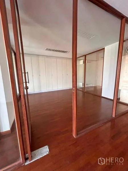 Home Office for rent or sale in Bang Phli, Samut Prakan - Entry to a glass-partition office room with white built-in cabinetry and wood flooring.