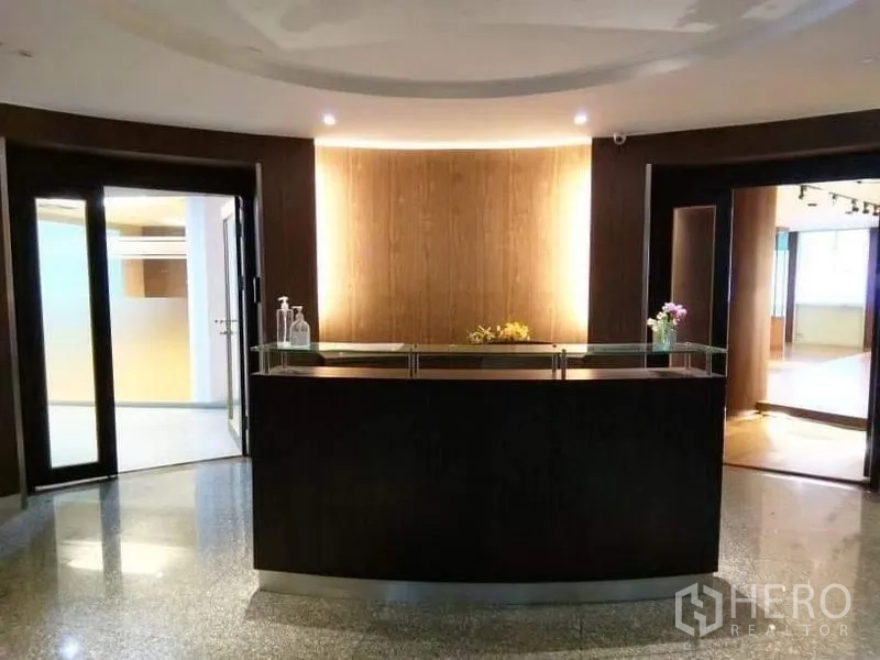 สำนักงาน ให้เช่า - โถงต้อนรับอบอุ่น เคาน์เตอร์ไม้สีเข้มโค้ง ไฟแบ็กไลต์ และพื้นหินขัด