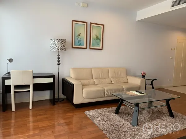 公寓 出租在Khlong Toei, Bangkok - 当代风格客厅，米色皮沙发、书桌、落地灯与地毯上的玻璃茶几。