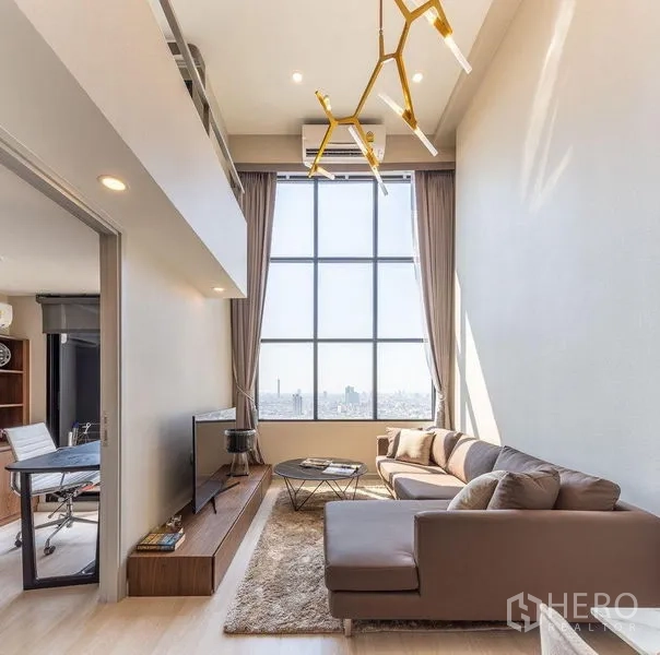คอนโด ให้เช่าในSathon, Bangkok - ห้องนั่งเล่นเพดานสูงสองชั้น หน้าต่างสูงจรดเพดาน โซฟาเข้ามุม โคมไฟสีทอง และวิวเมืองกว้างไกล