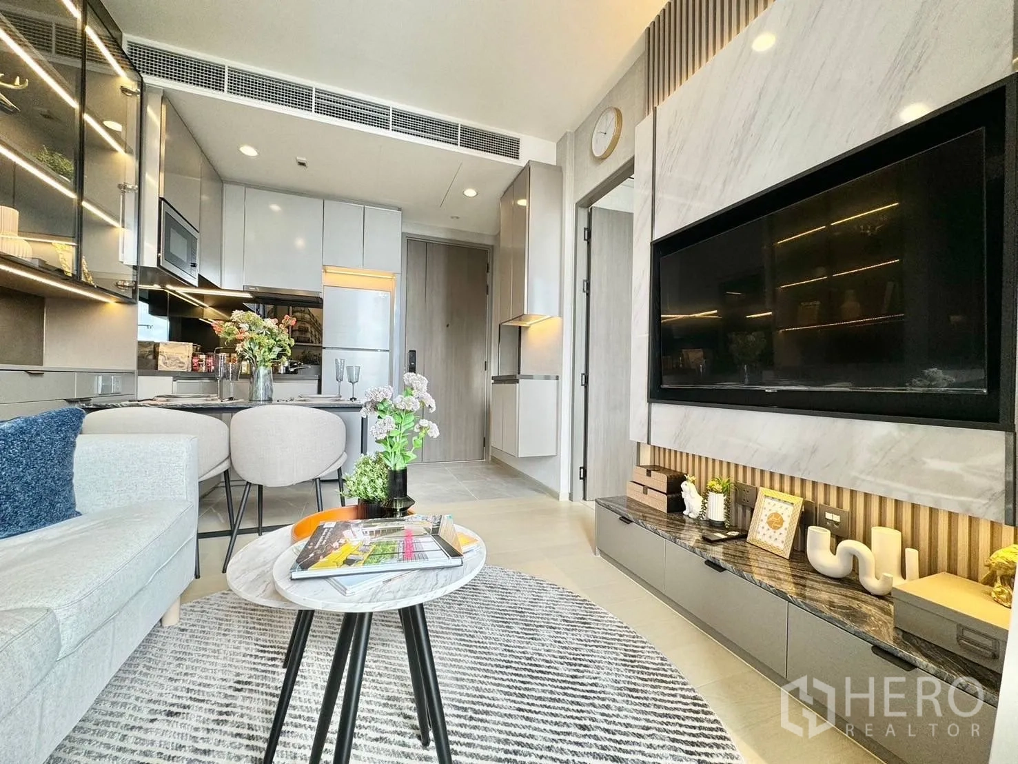 คอนโด for rent in Ratchathewi, Bangkok - ห้องนั่งเล่นแบบโอเพ่นมีโซฟา ผนังทีวีลายหินอ่อน และครัวกะทัดรัดพร้อมโต๊ะทานอาหารสำหรับสองคน