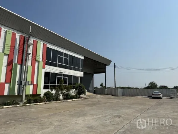 Warehouse for rent in Samut Prakan - Wide concrete yard and parking beside the warehouse with colorful facade panels and perimeter fence.